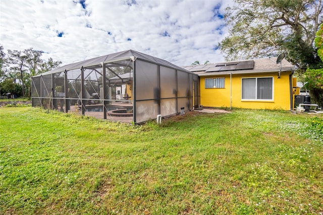 rear view of house with solar panels, a yard, and a lanai