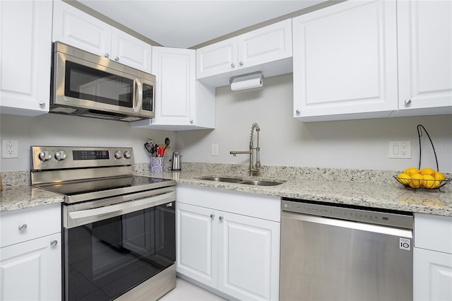 kitchen featuring stainless steel appliances, light stone countertops, white cabinetry, and a sink