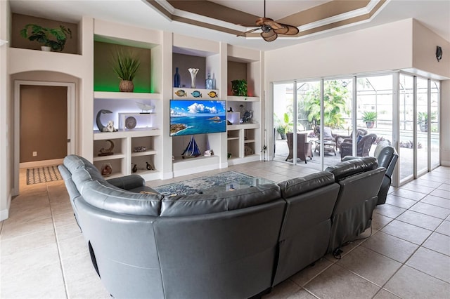 living room featuring built in shelves, ceiling fan, a tray ceiling, and light tile patterned floors