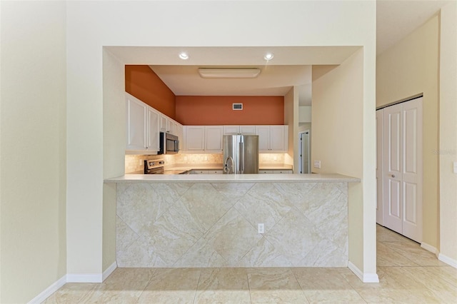 kitchen featuring white cabinets, kitchen peninsula, appliances with stainless steel finishes, and tasteful backsplash