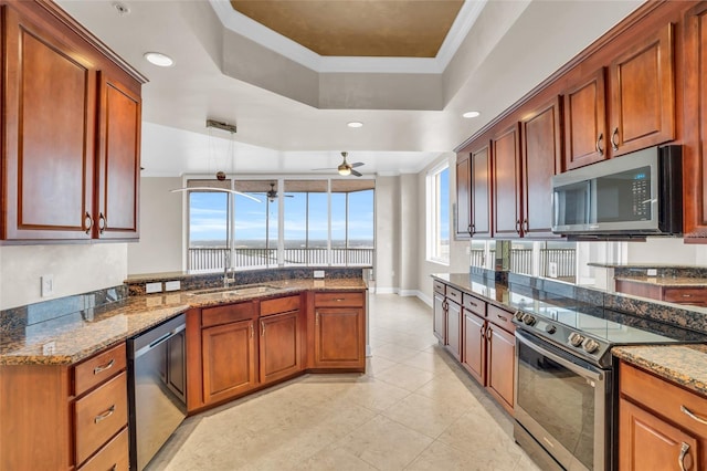 kitchen with ornamental molding, stainless steel appliances, ceiling fan, sink, and dark stone countertops