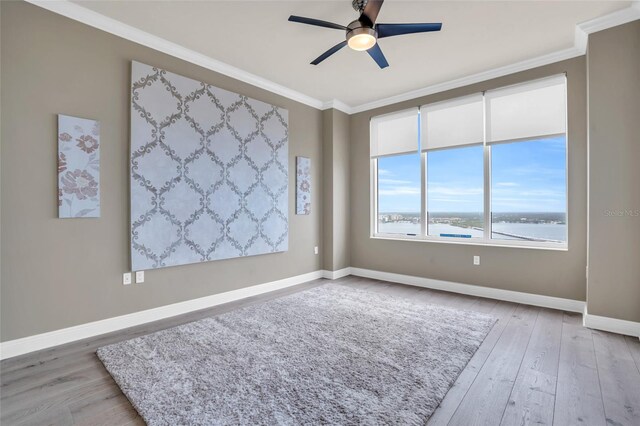 spare room featuring ceiling fan, crown molding, a water view, and light wood-type flooring