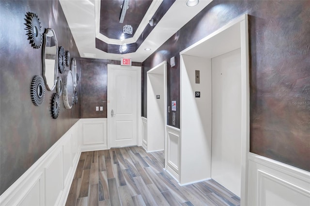 hall with a tray ceiling, elevator, and light hardwood / wood-style flooring