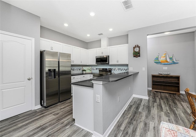 kitchen with appliances with stainless steel finishes, dark hardwood / wood-style floors, white cabinets, and kitchen peninsula