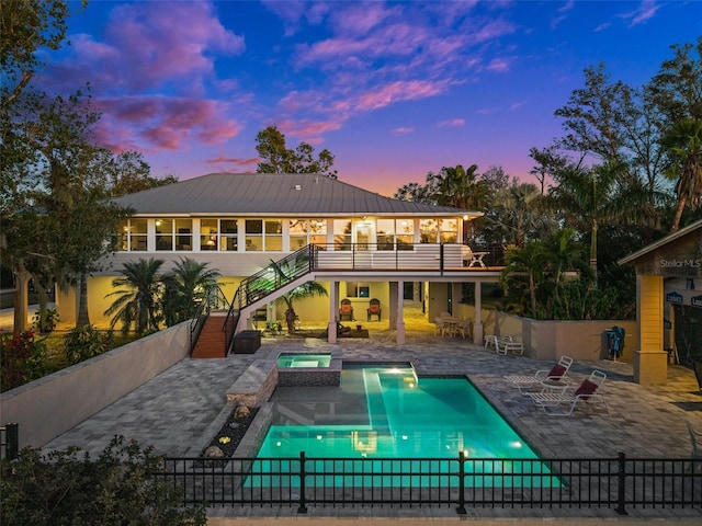 pool at dusk featuring an in ground hot tub, a sunroom, and a patio area