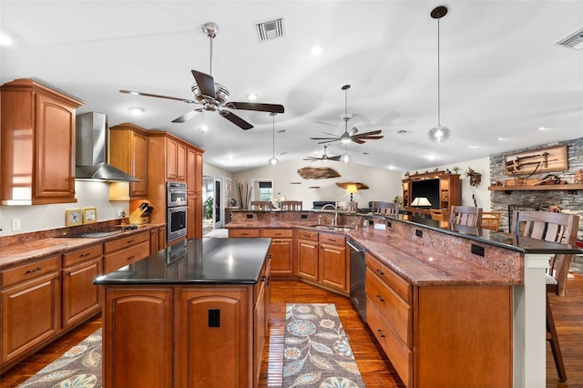 kitchen featuring a spacious island, a breakfast bar area, decorative light fixtures, appliances with stainless steel finishes, and wall chimney range hood