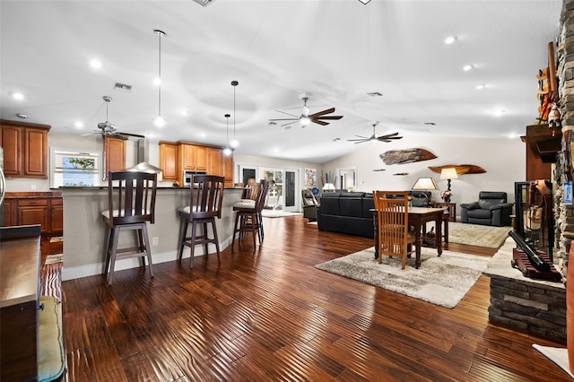 living room featuring ceiling fan, dark hardwood / wood-style floors, vaulted ceiling, and a stone fireplace