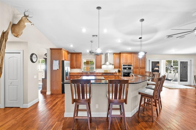 kitchen with pendant lighting, a breakfast bar area, wall chimney exhaust hood, and appliances with stainless steel finishes