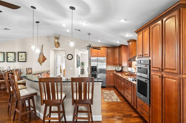 kitchen with dark wood-type flooring, a breakfast bar, decorative light fixtures, stainless steel appliances, and a kitchen island with sink