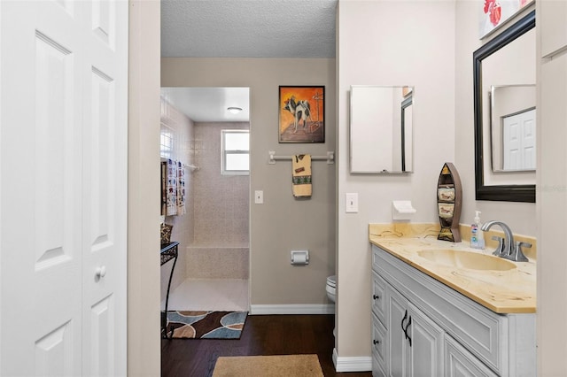 bathroom featuring toilet, a textured ceiling, a tile shower, vanity, and hardwood / wood-style flooring