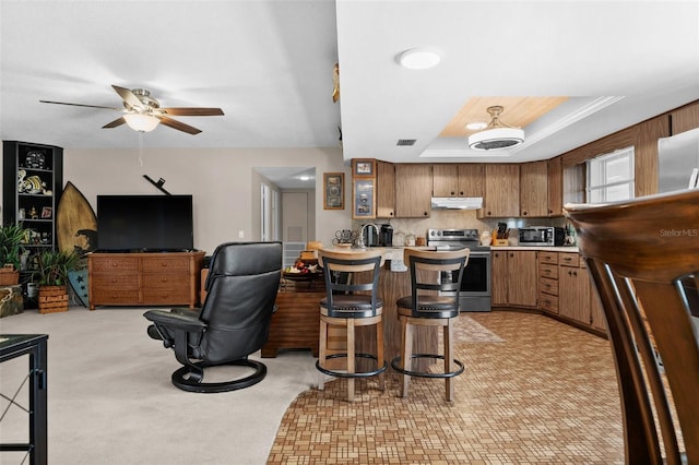 kitchen featuring a breakfast bar area, ceiling fan, a tray ceiling, stainless steel electric stove, and kitchen peninsula