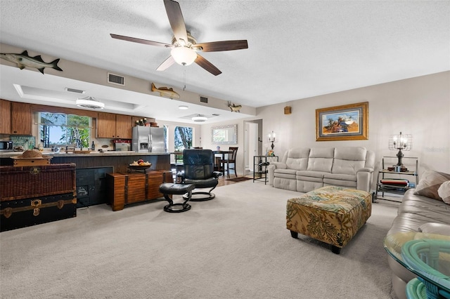 living room with ceiling fan, light carpet, a textured ceiling, and a tray ceiling