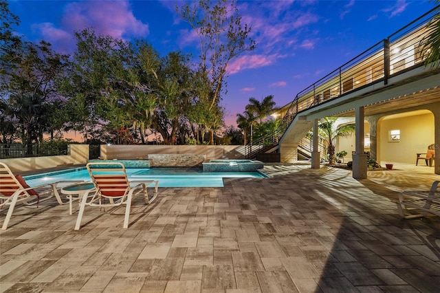 pool at dusk featuring an in ground hot tub and a patio