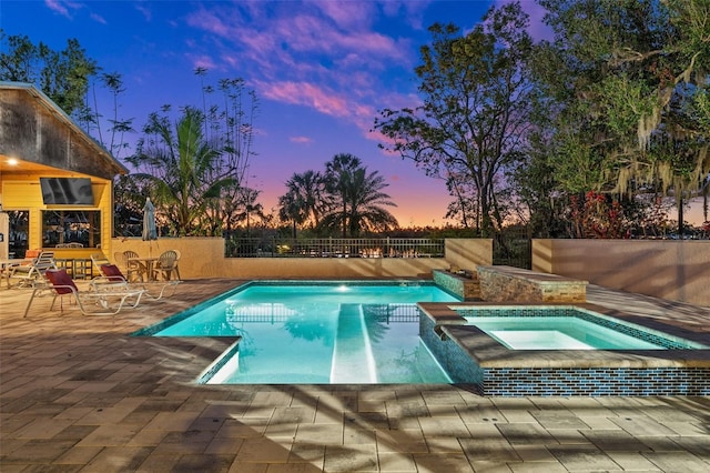 pool at dusk featuring an in ground hot tub and a patio