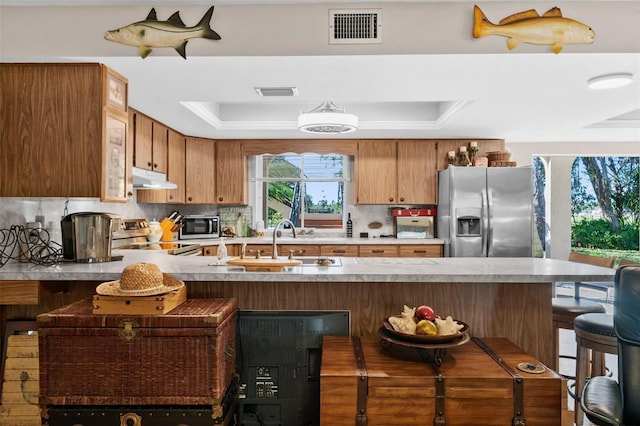 kitchen featuring sink, stainless steel appliances, a tray ceiling, a kitchen bar, and kitchen peninsula