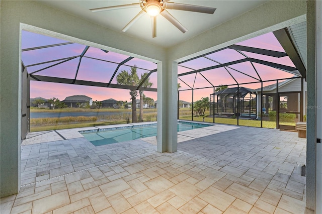 pool at dusk with a lanai, a patio area, and ceiling fan