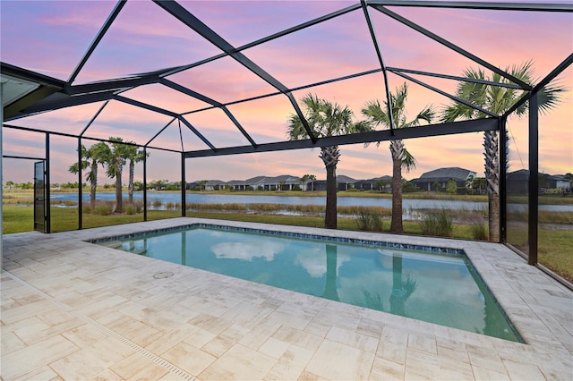 pool at dusk with a lanai, a patio area, and a water view