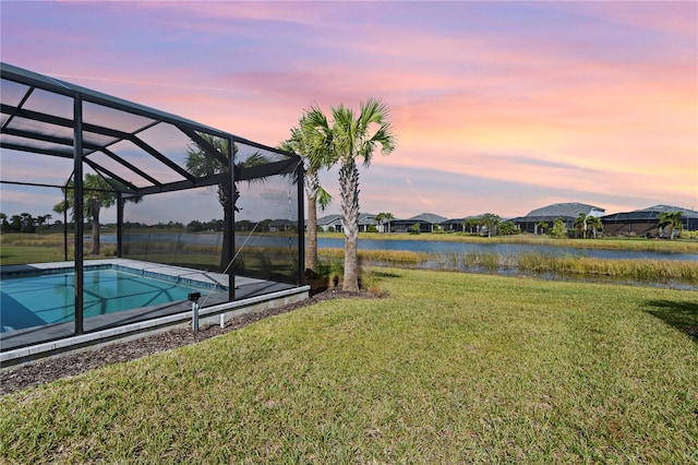 yard at dusk with a water view and glass enclosure