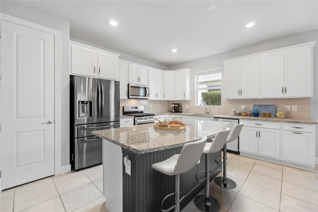 kitchen featuring white cabinetry, a kitchen island, stainless steel appliances, and light stone counters