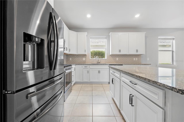 kitchen featuring white cabinets, backsplash, stainless steel appliances, and light stone countertops