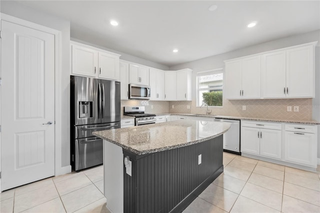 kitchen with white cabinets, a kitchen island, light stone counters, and stainless steel appliances