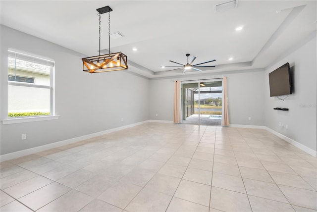 tiled empty room featuring a raised ceiling, a wealth of natural light, and ceiling fan