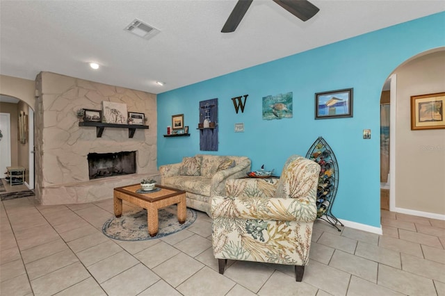 living room with light tile patterned floors, a textured ceiling, and a stone fireplace