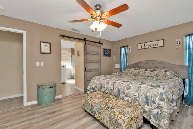 bedroom with a barn door, ceiling fan, and light hardwood / wood-style flooring