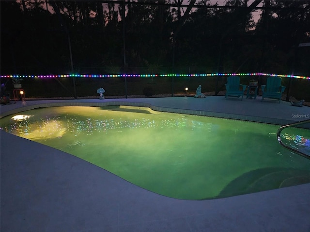 pool at night featuring a patio area