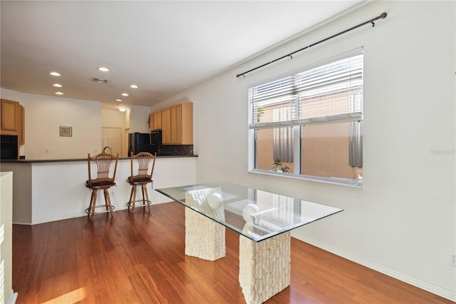 kitchen featuring black appliances, dark hardwood / wood-style floors, a kitchen bar, and kitchen peninsula