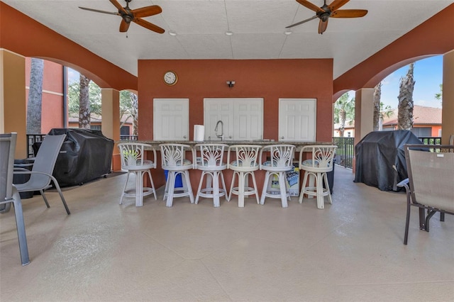 view of patio with ceiling fan, area for grilling, and a wet bar