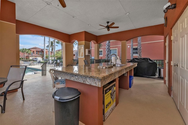 kitchen with a textured ceiling, ceiling fan, sink, and an island with sink