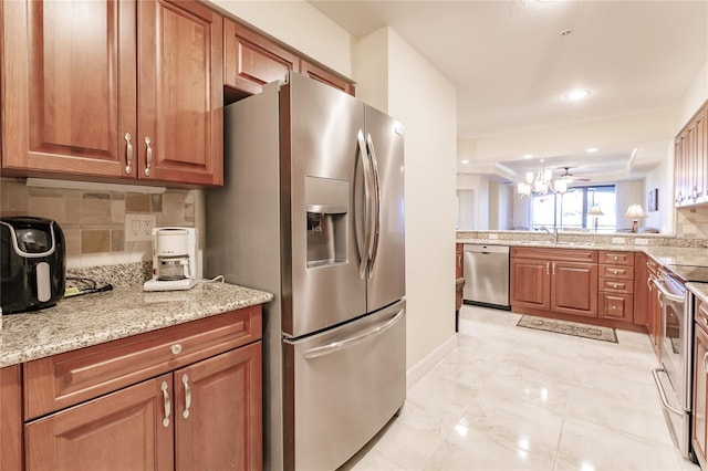 kitchen featuring sink, decorative backsplash, light stone countertops, appliances with stainless steel finishes, and a notable chandelier