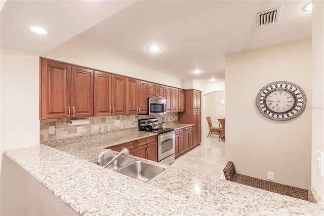 kitchen featuring decorative backsplash, kitchen peninsula, light stone countertops, stainless steel appliances, and sink