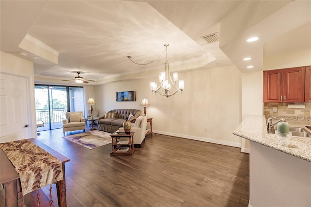 living room with a tray ceiling, sink, dark wood-type flooring, and ceiling fan with notable chandelier