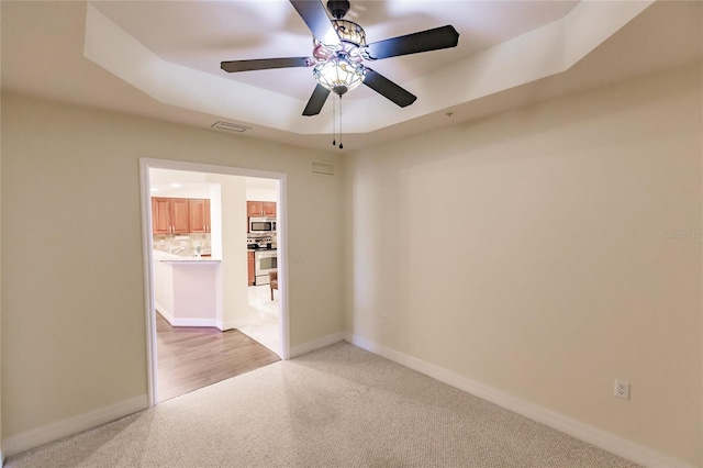 carpeted spare room with ceiling fan and a tray ceiling