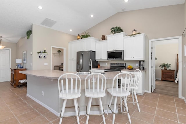 kitchen with white cabinets, appliances with stainless steel finishes, a large island with sink, and lofted ceiling