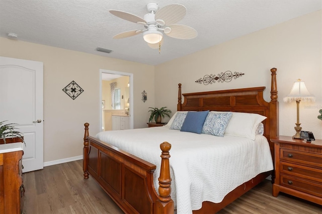 bedroom with a textured ceiling, connected bathroom, hardwood / wood-style flooring, and ceiling fan