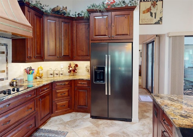 kitchen with light stone countertops, stainless steel fridge, tasteful backsplash, and custom range hood