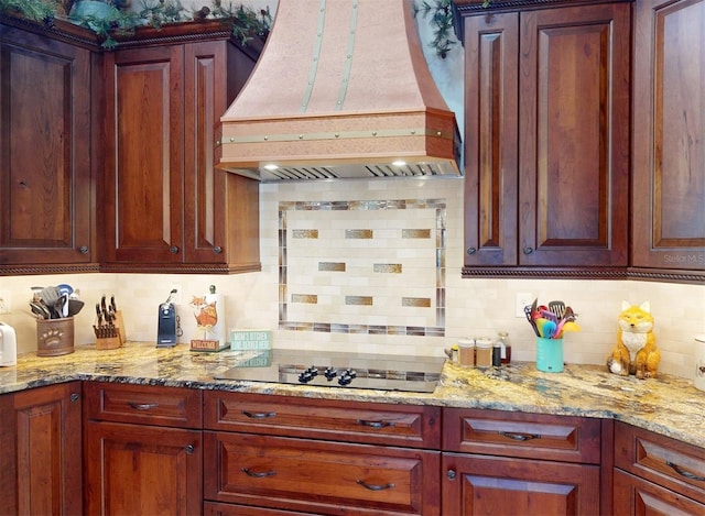 kitchen with light stone countertops, premium range hood, tasteful backsplash, and black electric cooktop