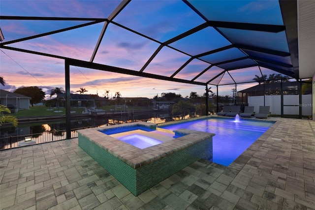 pool at dusk with an in ground hot tub, a patio, and a lanai