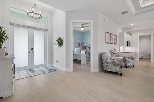 foyer with french doors, ceiling fan with notable chandelier, crown molding, washing machine and clothes dryer, and light hardwood / wood-style floors