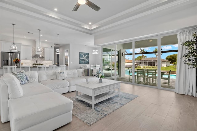 living room with a tray ceiling, light hardwood / wood-style flooring, ceiling fan, and crown molding