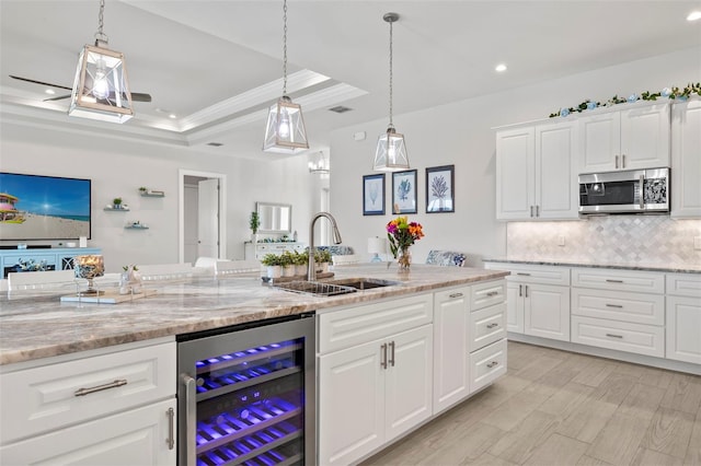 kitchen featuring a raised ceiling, sink, light stone counters, white cabinetry, and beverage cooler