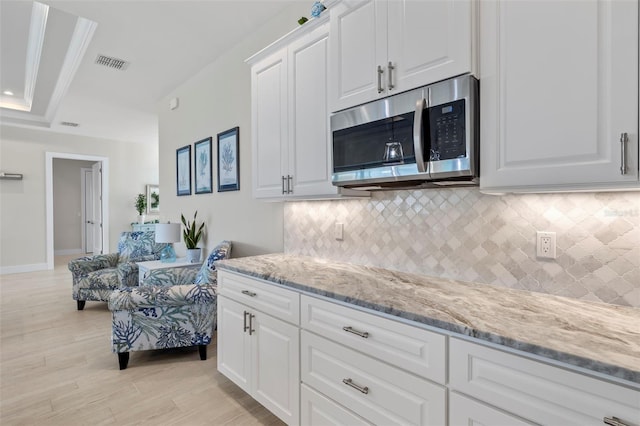 kitchen featuring tasteful backsplash, white cabinetry, light stone counters, and light hardwood / wood-style floors