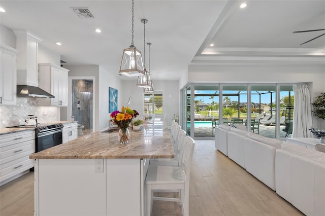 kitchen featuring pendant lighting, white cabinets, a spacious island, electric range, and light wood-type flooring