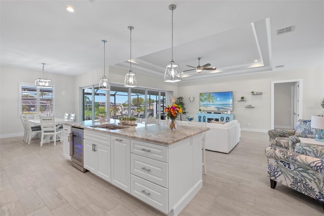 kitchen featuring light stone counters, ceiling fan, sink, a center island with sink, and white cabinetry