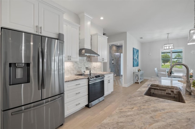 kitchen with white cabinets, sink, wall chimney exhaust hood, appliances with stainless steel finishes, and light hardwood / wood-style floors