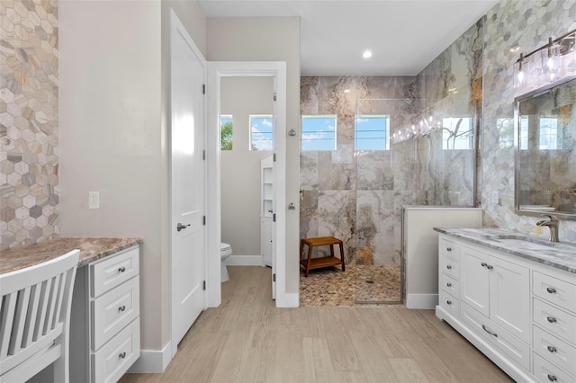 bathroom with a tile shower, vanity, wood-type flooring, and toilet