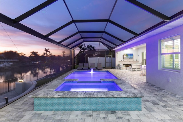 pool at dusk featuring an in ground hot tub, a patio, and a lanai